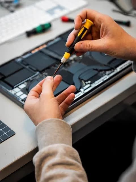 Mão com chave de precisão trabalhando dentro de um notebook aberto, com a bateria à mostra.