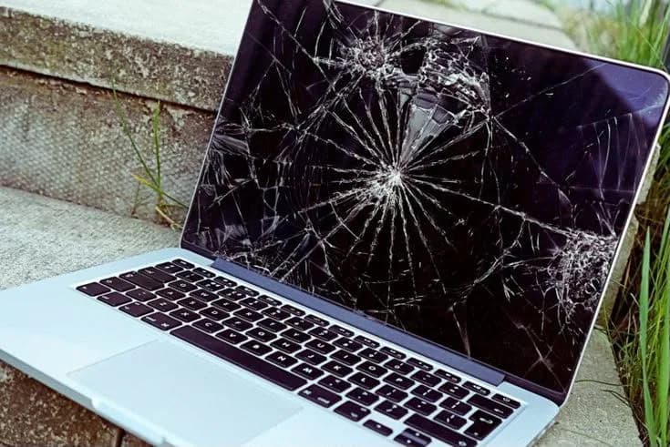 MacBook aberto com o vidro da tela trincado em teia a partir do centro.